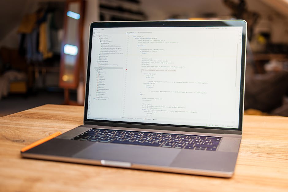 A person using a laptop computer with a black screen and a visible keyboard, positioned on a plain white surface. The laptop's display shows lines of code or text in a code editor with various tabs an